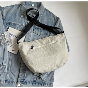 Beige crescent nylon crossbody bag with adjustable strap on blue denim jacket