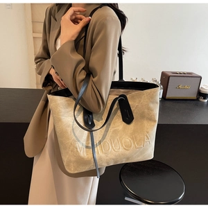 Detail of beige textured tote bag featuring embossed MEIDUOLA logo and black straps