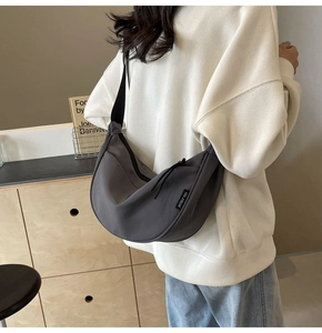 Detail of dark grey crescent crossbody bag showing nylon texture and branded woven label