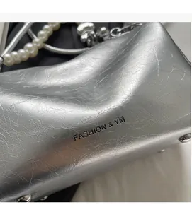 Details einer silbernen Tasche mit Faltenstruktur, Perlenriemen und Metallnieten am Boden