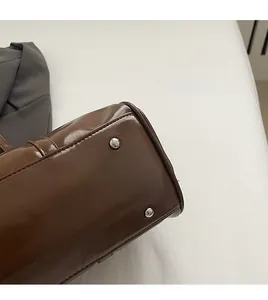 Detailed view of dark brown glossy leather bag bottom with protective silver rivets