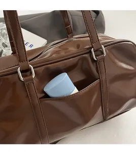 Close-up of brown glossy boston bag featuring a functional front pocket for storage
