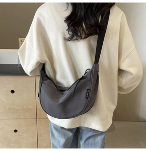 Close-up of grey crescent crossbody bag with adjustable black strap and brand tag