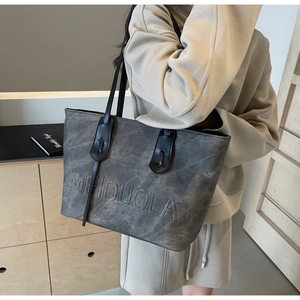 Detail showing grey textured tote bag with embossed lettering and black handles