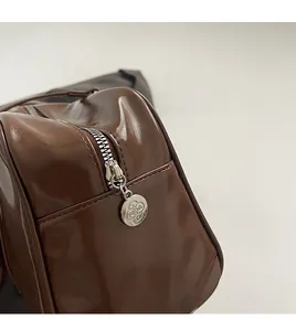 Detail of silver metal zipper with engraved floral charm on dark brown glossy bag