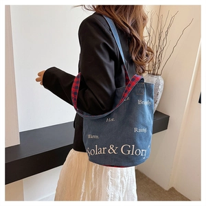 Dettaglio borsa tote in denim con manico a quadri rosso-blu e stampa grafica