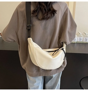 Detail of a creamy white crescent bag with wide black strap shown on a model