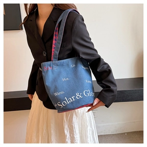 Dettaglio della borsa tote in denim con tracolla a quadri rossi e accenti grafici