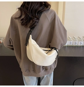 White dumpling-style crossbody bag with contrast black wide strap shown on a model