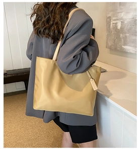 Detail of khaki nylon tote bag with leather straps and side tag on shoulder