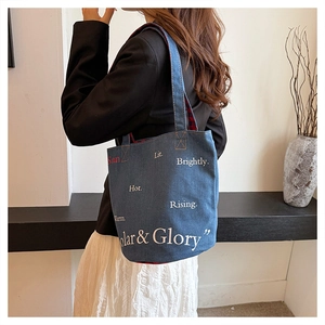 Dettaglio della borsa tote in denim blu scuro con scritte artistiche indossata da modella
