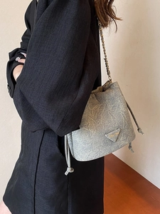 Gray drawstring bucket bag with chic metal logo and chain strap worn on black blazer