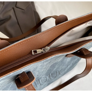 Detail of grey-blue textured fabric tote bag with brown leather handles and metal zipper