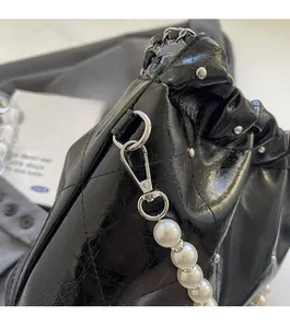 Detail of silver clasp and white pearl strap on black quilted oil wax leather bag
