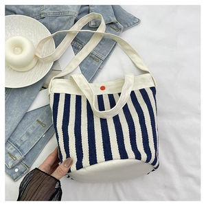 Détail du sac seau en toile rayée bleue avec poignées blanches et bouton rouge chic