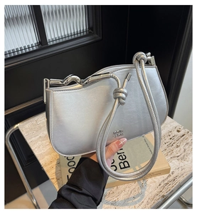 Detail of silver metallic handbag featuring wave-shaped handle and knot shoulder strap