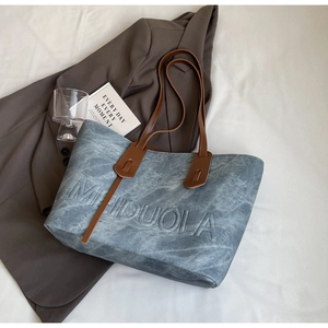 Detail of light blue textured tote bag with embossed lettering and brown leather straps