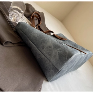 Detail view of large grey-blue tote bag with brown leather handles and embossed logo