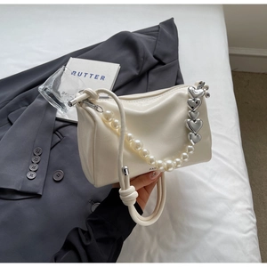 Detail der cremefarbenen Tasche mit großen Perlen und Herzkette auf grauem Blazer