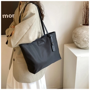 Detail of Carolmarti black nylon tote bag with leather logo patch and thin shoulder strap