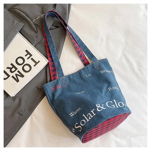 Dettaglio borsa tote in denim scuro con scritte artistiche e manici a scacchi rossi