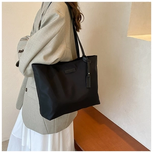 Detail shot of a black Oxford tote bag with brand logo plaque and hanging tag accessory