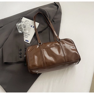 Macro shot of dark brown glossy pillow bag with silver hardware on a grey suit jacket