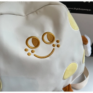 Detailed view of canvas bag featuring gold embroidered smiley face and yellow fabric patches
