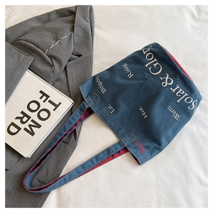 Dettaglio della borsa tote in denim con fodera a quadri rosso e blu e scritte