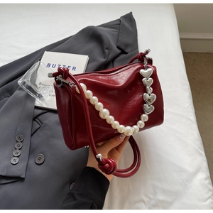 Detail der dunkelroten Lackledertasche mit Perlenriemen und silbernen Herzanhängern