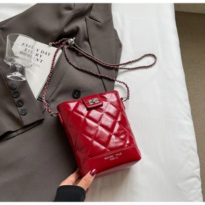 Detail of red quilted bucket bag with glossy finish, chain strap and metallic lock