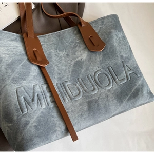 Detailed view of MEIDUOLA embossed texture on a blue washed canvas tote bag with leather strap