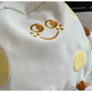 Close-up of a white canvas bag featuring a yellow embroidered smiley face and polka dots