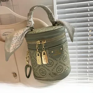 Détail d'un sac seau vert cylindrique avec gaufrage de lettres et foulard fleuri