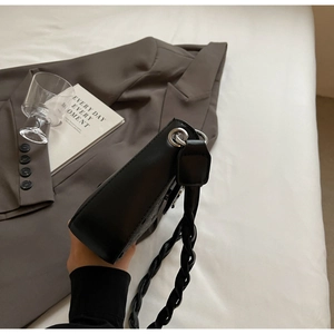 Detail der schwarzen Leder-Unterarmtasche mit dickem geflochtenem Riemen und Metallringen