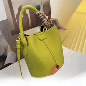 Détail d'un sac seau en cuir grainé vert avec un élégant foulard en soie sur la poignée