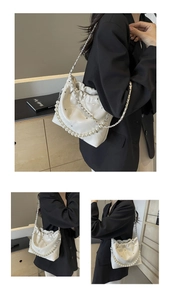 Close-up of white glossy quilted shoulder bag with pearl chain and rivet details