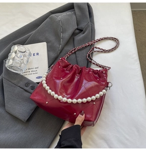 Detail of red quilted bucket bag featuring a pearl handle and chain strap
