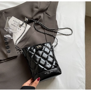 Detailed view of black quilted bucket bag with silver clasp and leather-woven chain strap