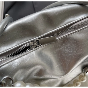 Detail einer silbernen Tasche mit Knitteroptik-Leder und einer Perlen-Zierkette