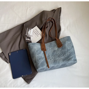 Detail of blue-grey textured tote bag featuring embossed logo and leather shoulder strap