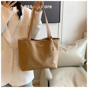 Detail of khaki oxford tote bag with Carolmanti logo held by a model in a white suit