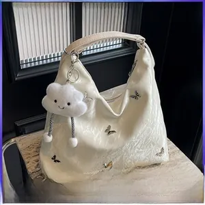 Détail du sac hobo plissé crème avec des papillons argentés et un porte-clé nuage doux