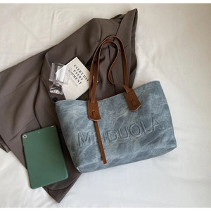 Detail view of retro blue textured tote bag with embossed letters and brown leather straps