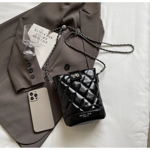 Close-up of black quilted chain bucket bag with metal twist lock and logo detail