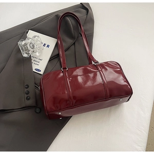 Detailed close-up of dark red glossy patent leather bag with silver protective base studs