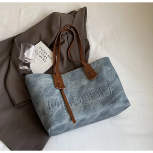 Detail of grey-blue tote bag featuring MEIDUOLA embossed lettering and brown leather handles
