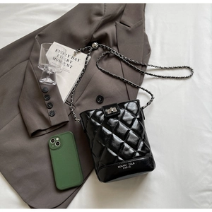 Detail of black quilted bucket bag featuring a silver twist lock and metal chain strap