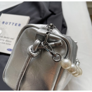 Detail der silbernen Metallic-Handtasche mit großen weißen Perlenanhänger und Beschlägen