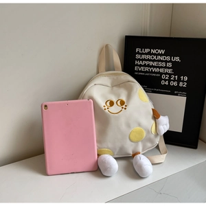 Detail of cute off-white canvas backpack with smiley embroidery beside a pink tablet